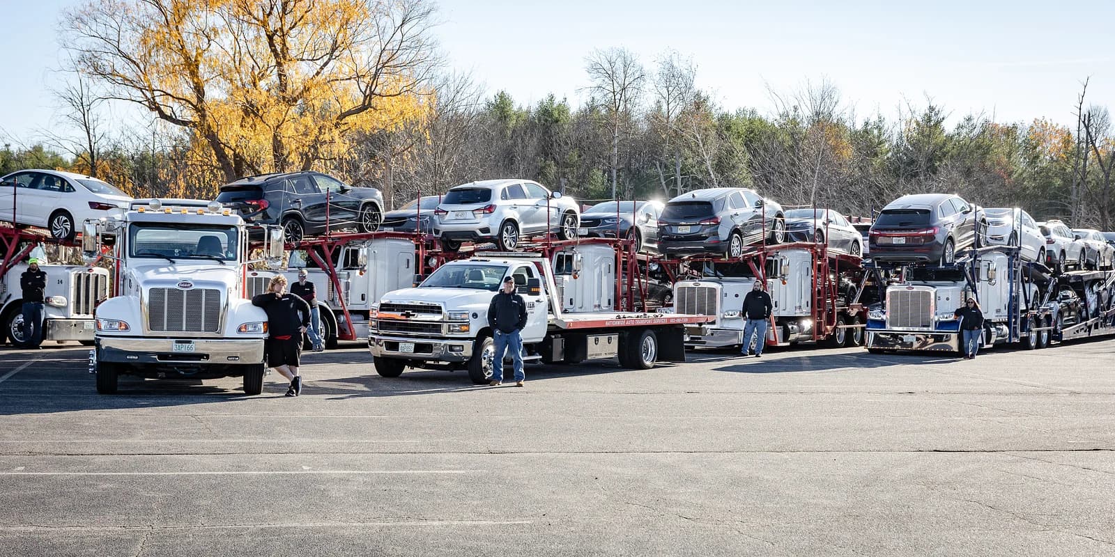 Dealership auto transport — Baier Transport drivers and multi-car carriers staged at a dealer yard with autumn foliage