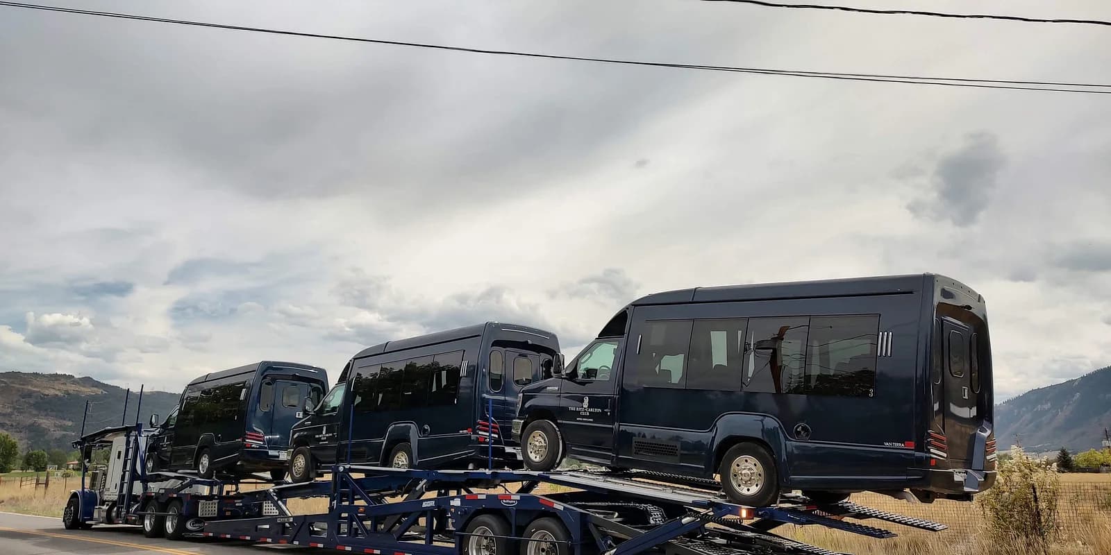 How auto transport works — Baier Transport open multi-car hauler in transit on a US highway carrying premium passenger vans