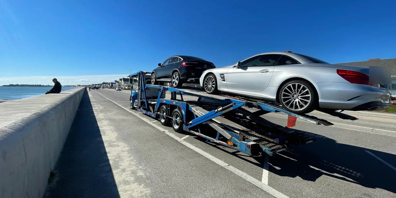 Baier Transport car carrier with a silver Mercedes on a coastal road, delivering a snowbird vehicle